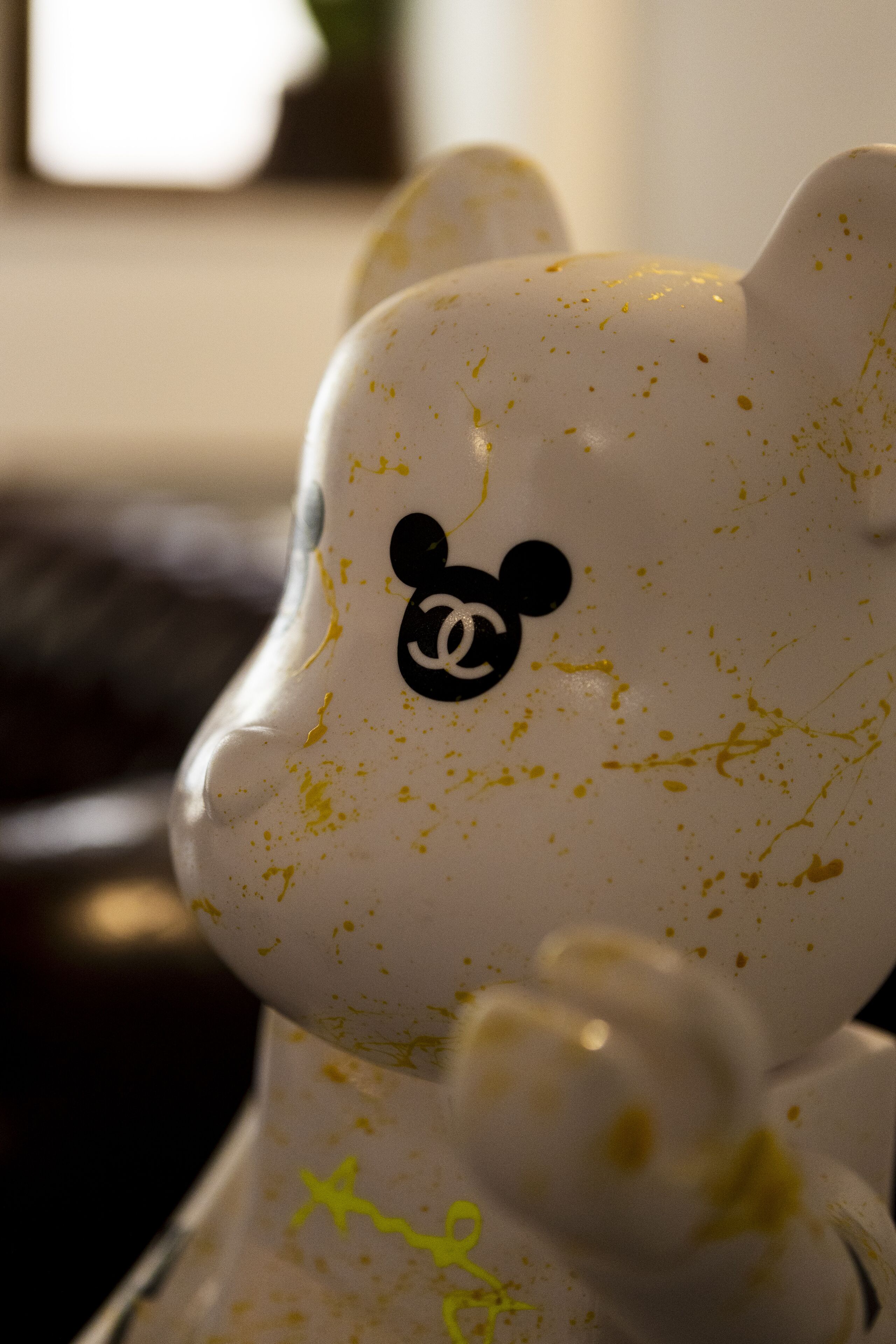 A white ceramic bear figurine with a Mickey Mouse logo and some yellow splatters.