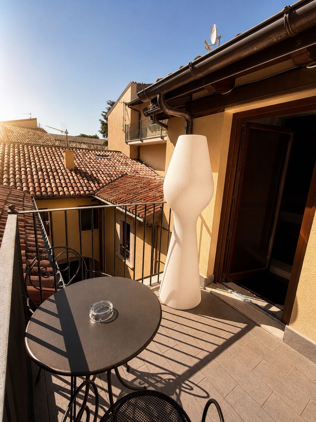Ein Balkon mit rundem Tisch, einem Stuhl und einer großen weißen Vase.