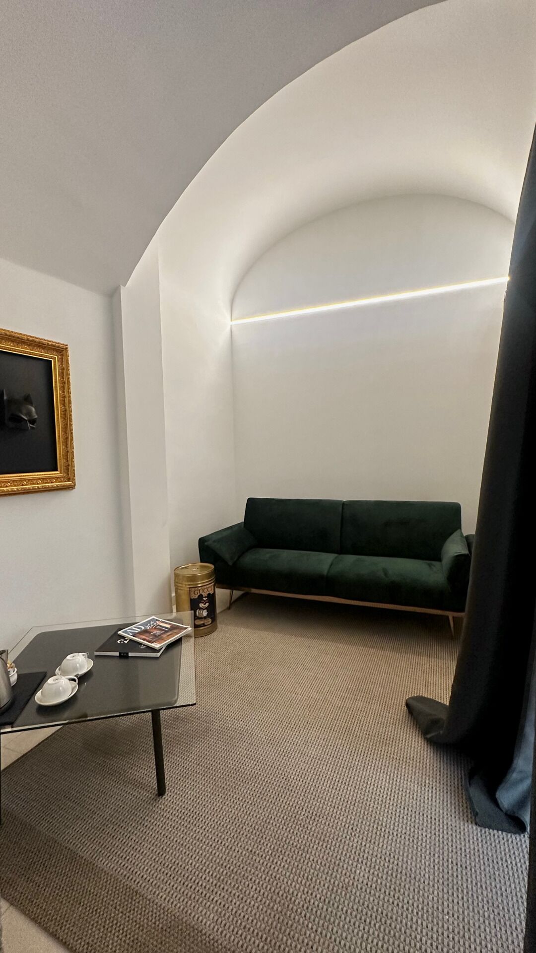 Una sala de estar moderna con una pared blanca curva, un sofá verde, una mesita con una revista y un cuadro enmarcado en la pared.