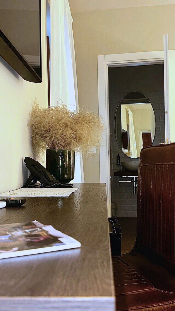 A wooden desk with a telephone, a vase with dried plants, and a magazine. A brown leather couch is visible to the right.