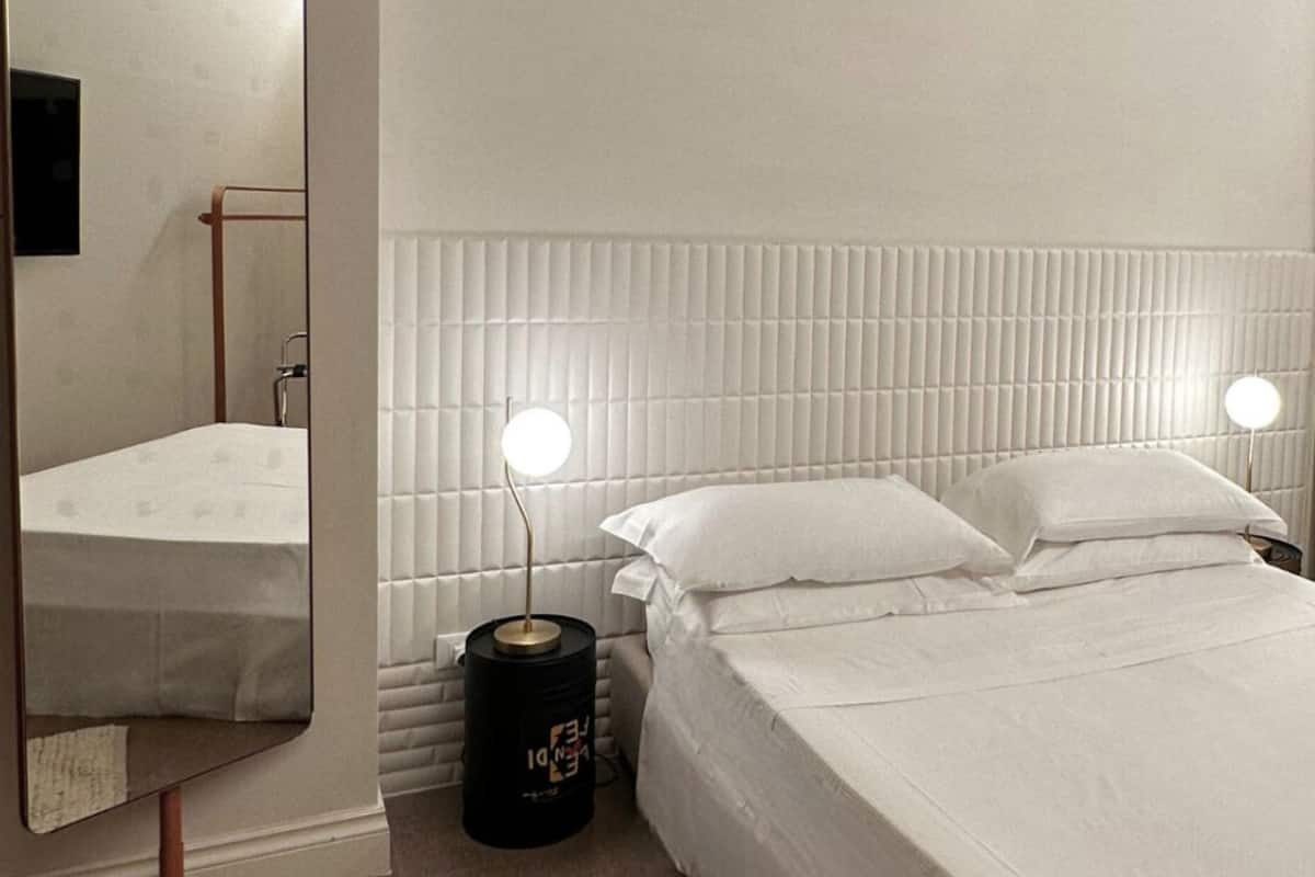 Ein modernes Hotelzimmer mit einem großen Bett, Nachttischlampen, einem Spiegel und einem strukturierten Teppich.