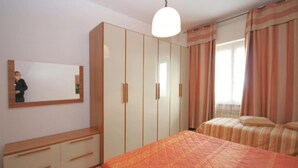 Une chambre avec un grand lit, une armoire, un miroir et une fenêtre avec des rideaux.
