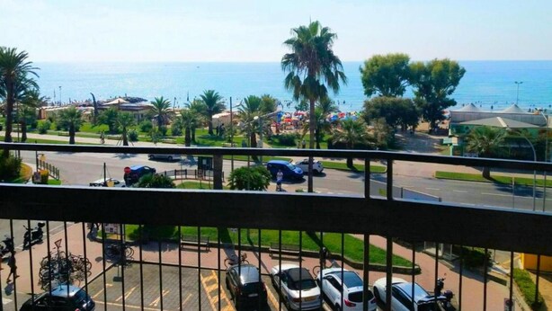 Un balcon avec vue sur une plage, des voitures garées et des palmiers.