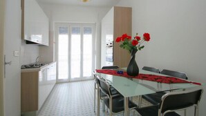 Un coin repas avec une table en verre, des chaises noires et un vase rempli de fleurs rouges.