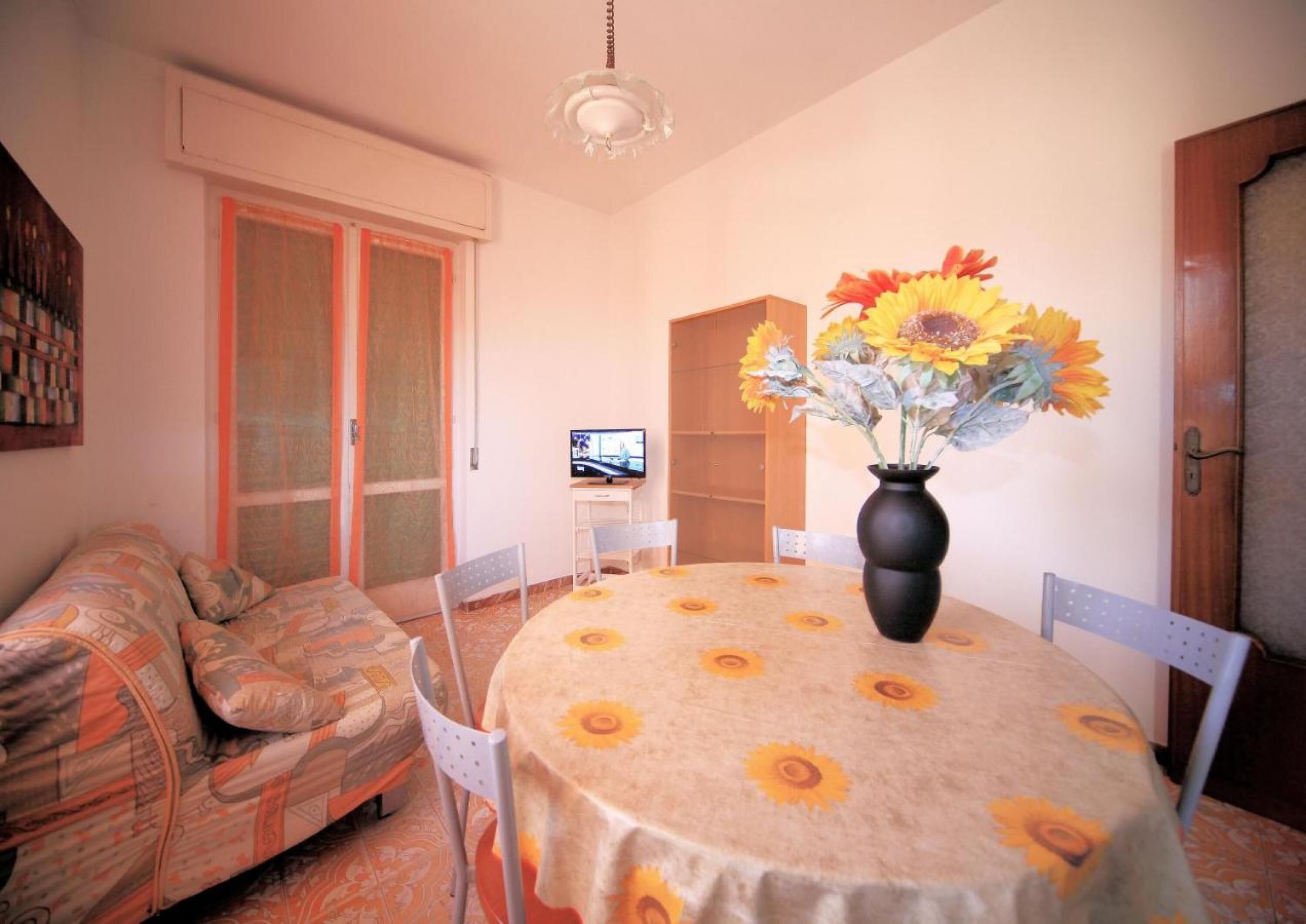 A cozy living room with a sofa, a round table with a sunflower tablecloth, and a vase with flowers.
