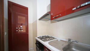 Uma cozinha compacta com armários vermelhos, fogão a gás, pia e lava-louças.