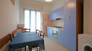 A compact kitchen with blue cabinets, a dining table with chairs, a washing machine, and a window with curtains. - Doria 6 Int 5 in Marina di Andora (Andora)