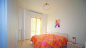 A bedroom with a bed, a nightstand, a lamp, a painting, and a door leading to another room.