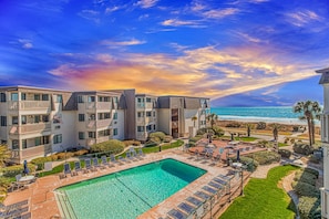 A multi-story hotel with a pool, outdoor seating, and a view of the ocean.