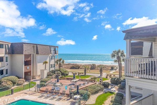 A beachfront hotel with a pool, lounge chairs, and a view of the ocean.