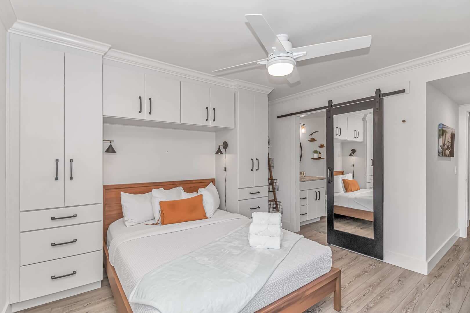 Een slaapkamer met een bed, witte kasten, een plafondventilator en een schuifdeurkast.