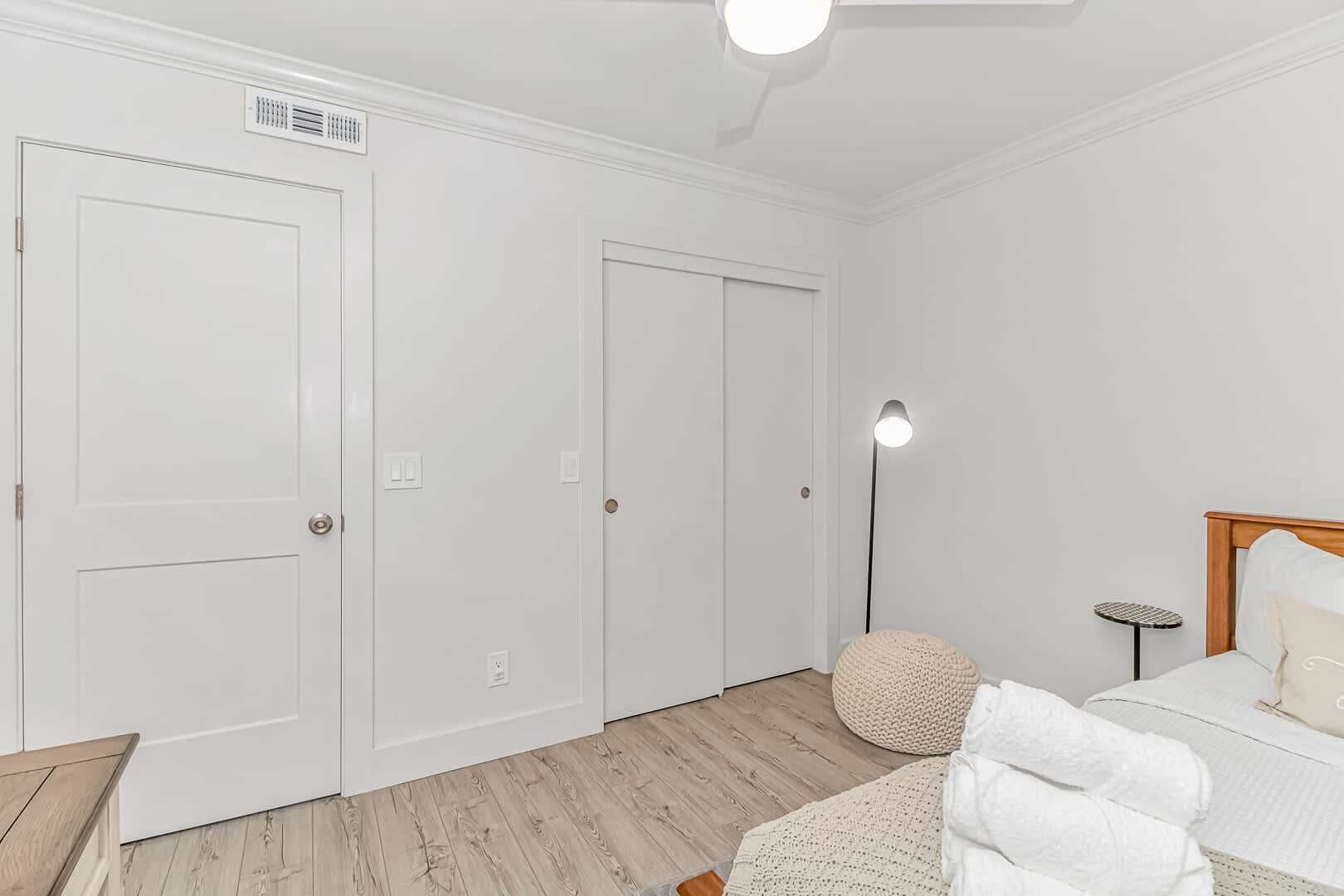 A bedroom with a bed, a bedside table, a floor lamp, and a closet with a ceiling fan.