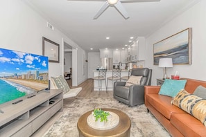 A modern living room with a TV, sofa, coffee table, and a dining area with chairs.