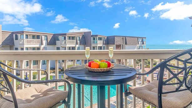 A balcony with a table, two chairs, a fruit bowl, and two glasses of champagne. - Ocean Forest Villas A-305 (Myrtle Beach)
