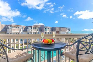 A balcony with a table, two chairs, a fruit bowl, and two glasses of champagne.