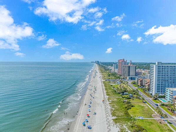 Enjoy the serene beachside views and stroll along the wide, sandy beach lined with umbrellas.