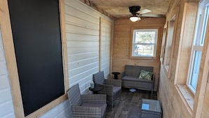 A wooden interior with a ceiling fan, a blackboard, wicker furniture, and a window.
