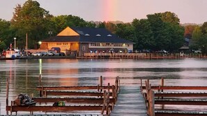 A wooden pier extending into calm water with a rainbow in the background.