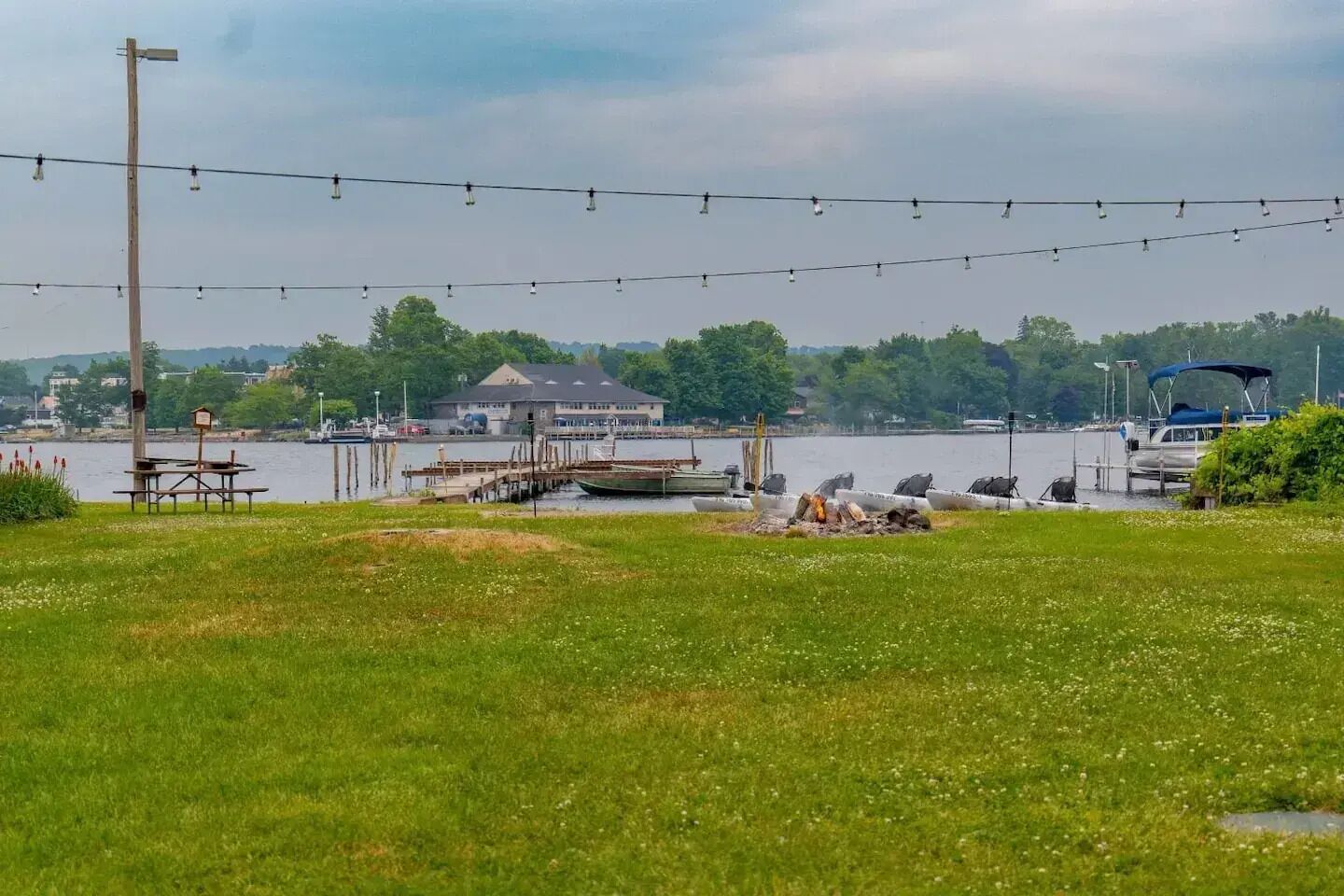 A lakeside view with a dock, picnic tables, and a building in the background.