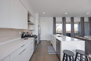 A modern kitchen with white cabinetry, a central island with stools, a stove, and a refrigerator.
