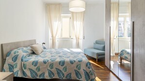 A bedroom with a bed, a chair, a mirror, and a window with curtains. - GuestHost - Hospital Riuniti - Lovely Apartment with Parking! (Livorno)