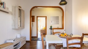 A dining area with a white table, wooden chairs, a fruit basket, and a hanging light fixture. - GuestHost - Hospital Riuniti - Lovely Apartment with Parking! (Livorno)