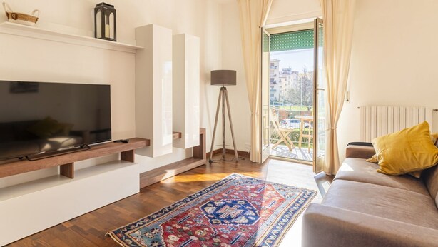 A living room with a TV, sofa, and a patterned rug. - GuestHost - Hospital Riuniti - Lovely Apartment with Parking! (Livorno)