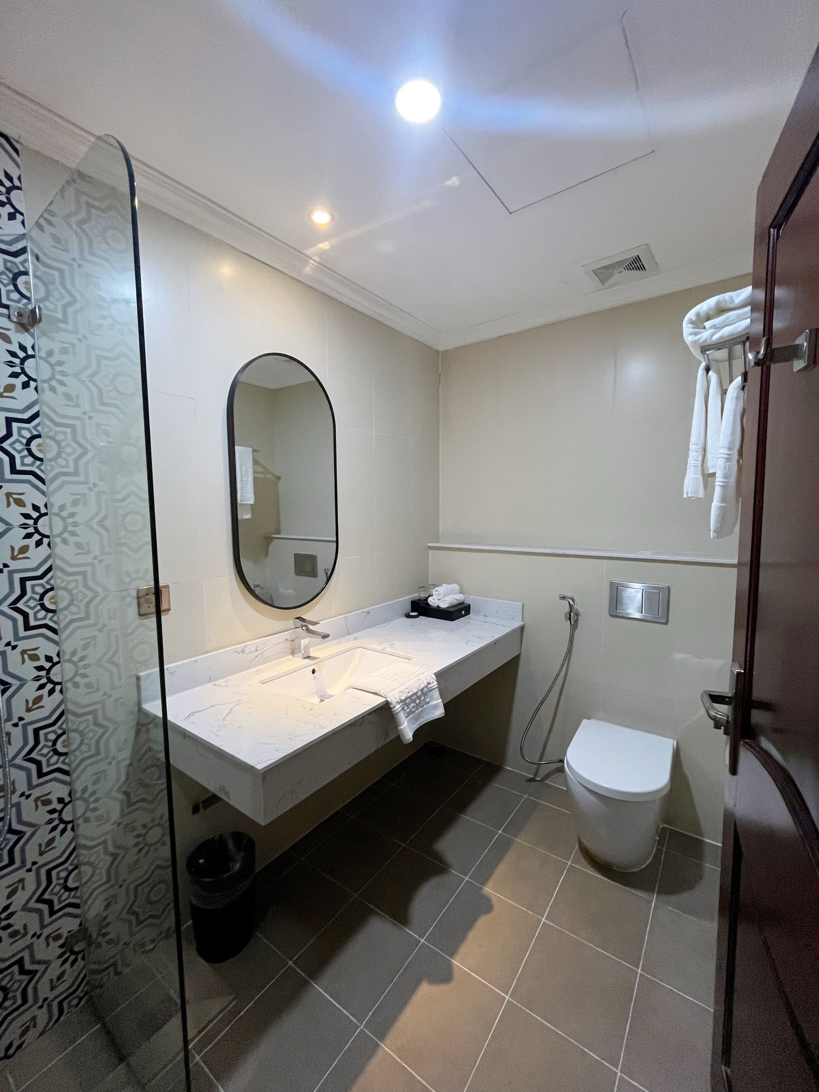 Un baño con cabina de ducha de vidrio, un lavabo blanco con una toalla, inodoro y espejo.