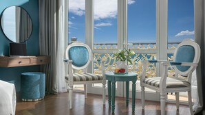 A room with a large window, a round mirror, a small table with a vase and fruit, and two upholstered chairs. - Paracel Beach Hotel (Da Nang)