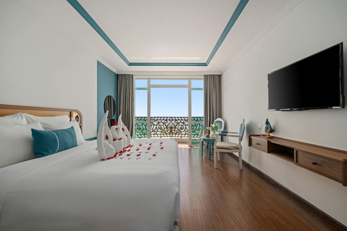 Ein Hotelzimmer mit einem großen Bett, einem Fernseher, einem Balkon mit Blick und einem Holzboden.