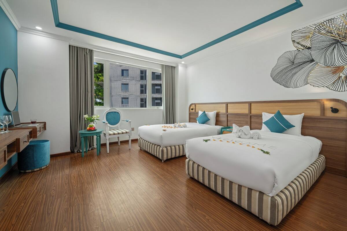 Ein Hotelzimmer mit zwei Betten, einem Schreibtisch, einem Stuhl, einem kleinen Tisch mit einer Vase und einem großen Fenster.