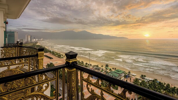 A balcony with ornate railings overlooking a beach with a sunset. - Paracel Beach Hotel (Da Nang)