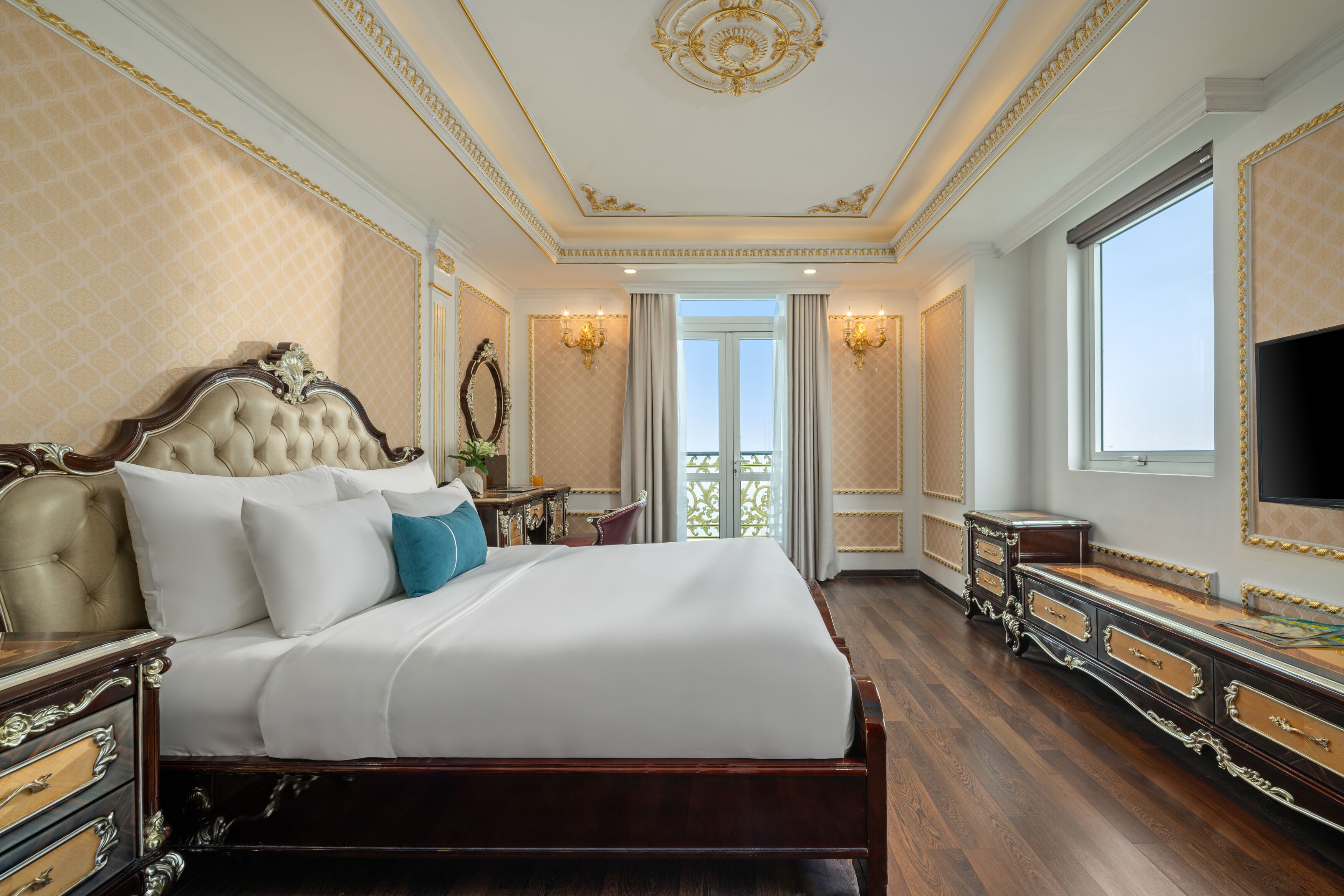 Un dormitorio lujoso con una cama grande, un tocador ornamentado y un televisor en la pared.