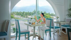 A dining area with a large arched window offering a view of palm trees and mountains. - Paracel Beach Hotel (Da Nang)