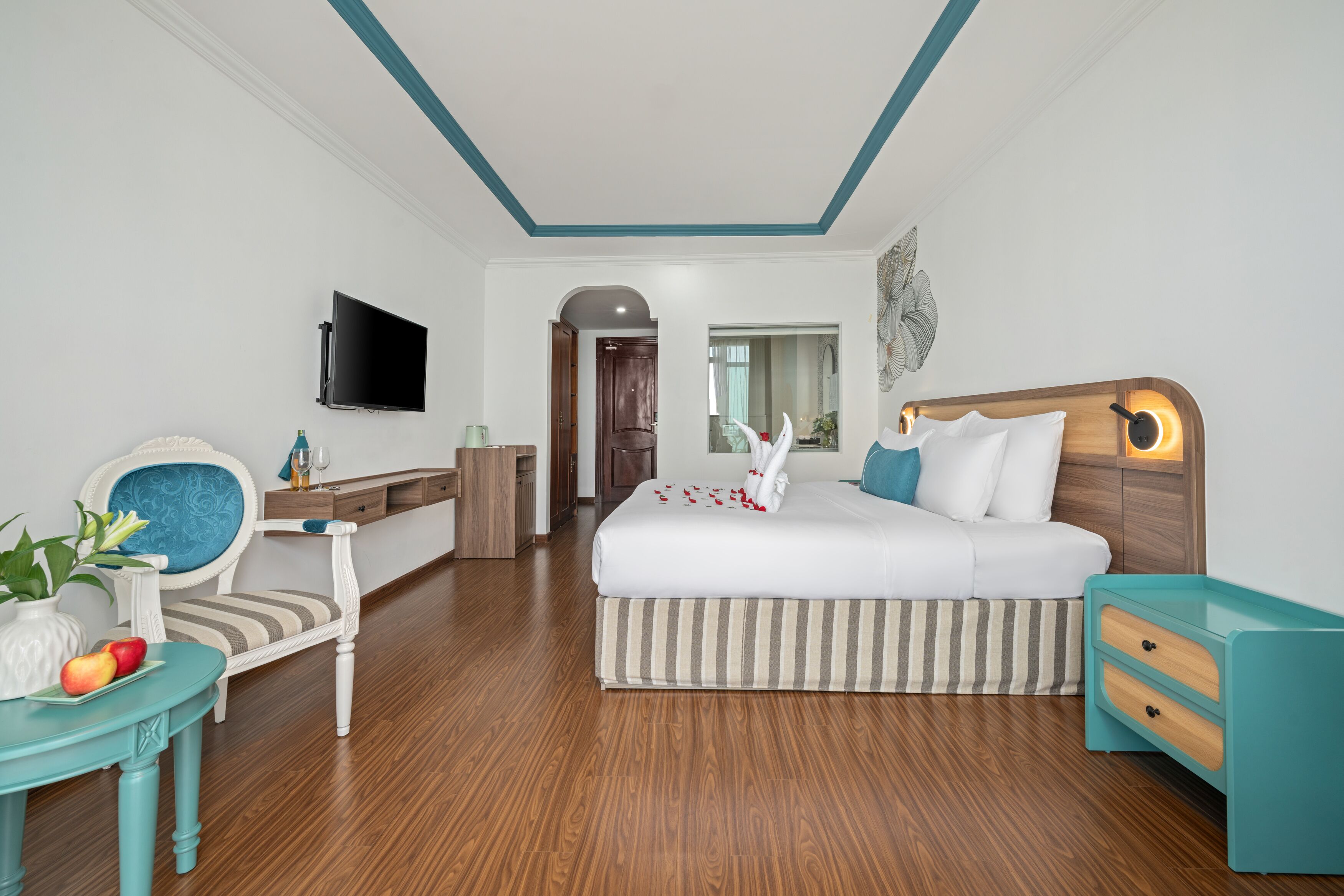 A hotel room with a bed, a TV, a desk, a chair, and a small table with fruit.