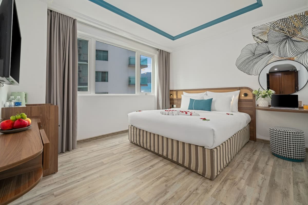 Ein Hotelzimmer mit Bett, Schreibtisch mit Obstschale, Fernseher und einem Vorhangfenster.