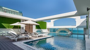 A modern outdoor swimming pool with lounge chairs and umbrellas, surrounded by a wooden deck and glass railings. - Paracel Beach Hotel (Da Nang)