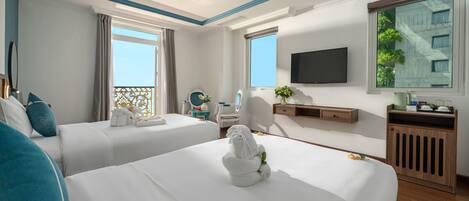 A hotel room with two beds, a TV, a balcony, and a view of a building.