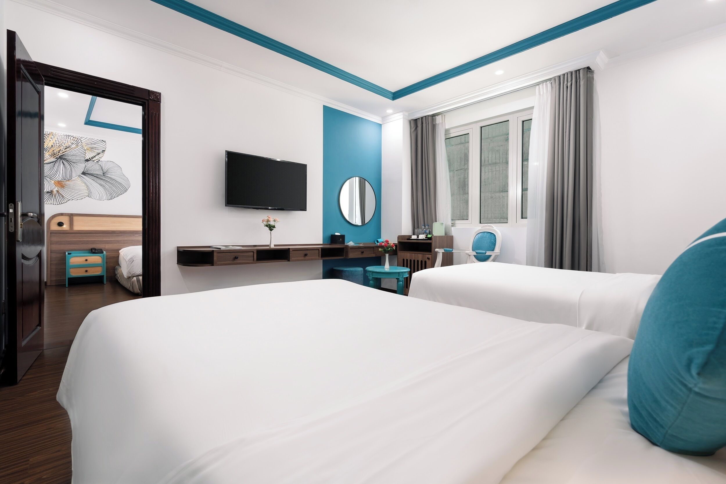 Een hotelkamer met twee bedden, een bureau, een televisie, een spiegel en een raam met gordijnen.