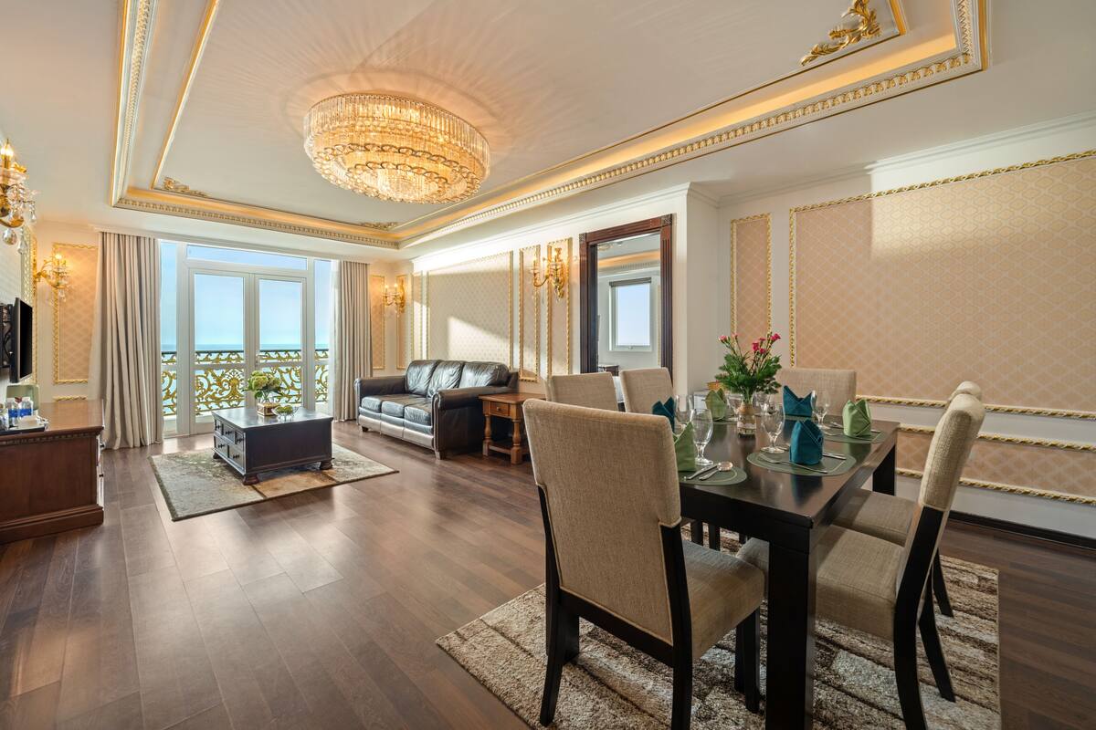 Ein geräumiges Wohnzimmer mit einer Chandelier, einem Sofa, einem Esstisch für vier Personen und einem Balkon mit Blick.