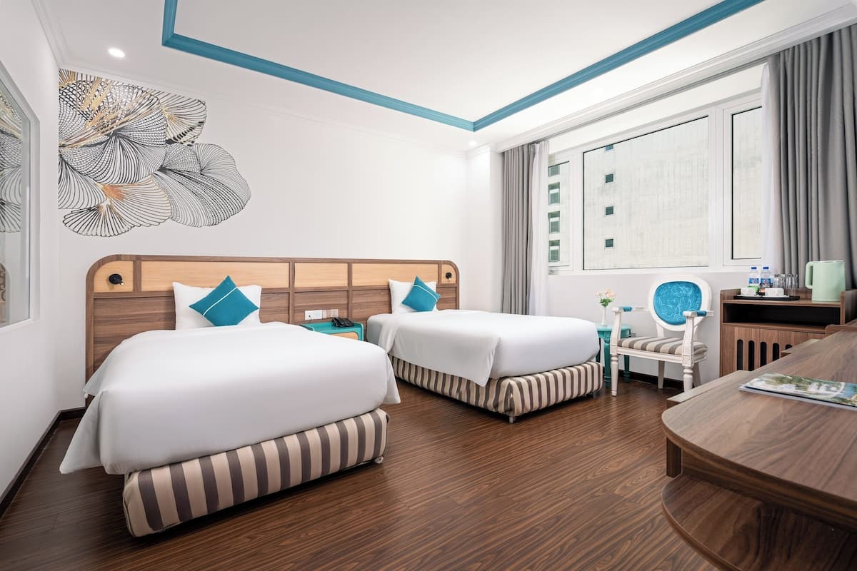 Ein Hotelzimmer mit zwei Betten, einem Holz-Kopfteil, einem Schreibtisch mit Stuhl, einem Fenster mit Vorhängen und einem Wanddekor.