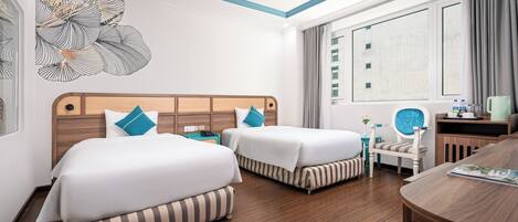A hotel room with two beds, a wooden headboard, a desk with a chair, a window with curtains, and a decorative wall piece.