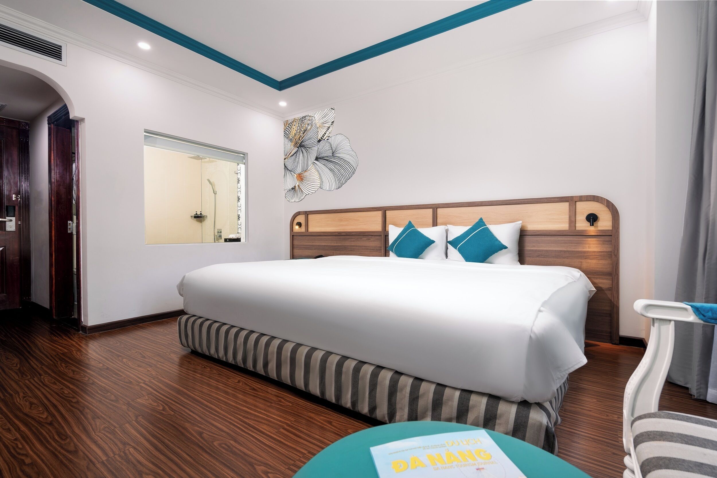 A hotel room with a large bed, a wooden headboard, a striped bench, a mirror, and a wall art piece.
