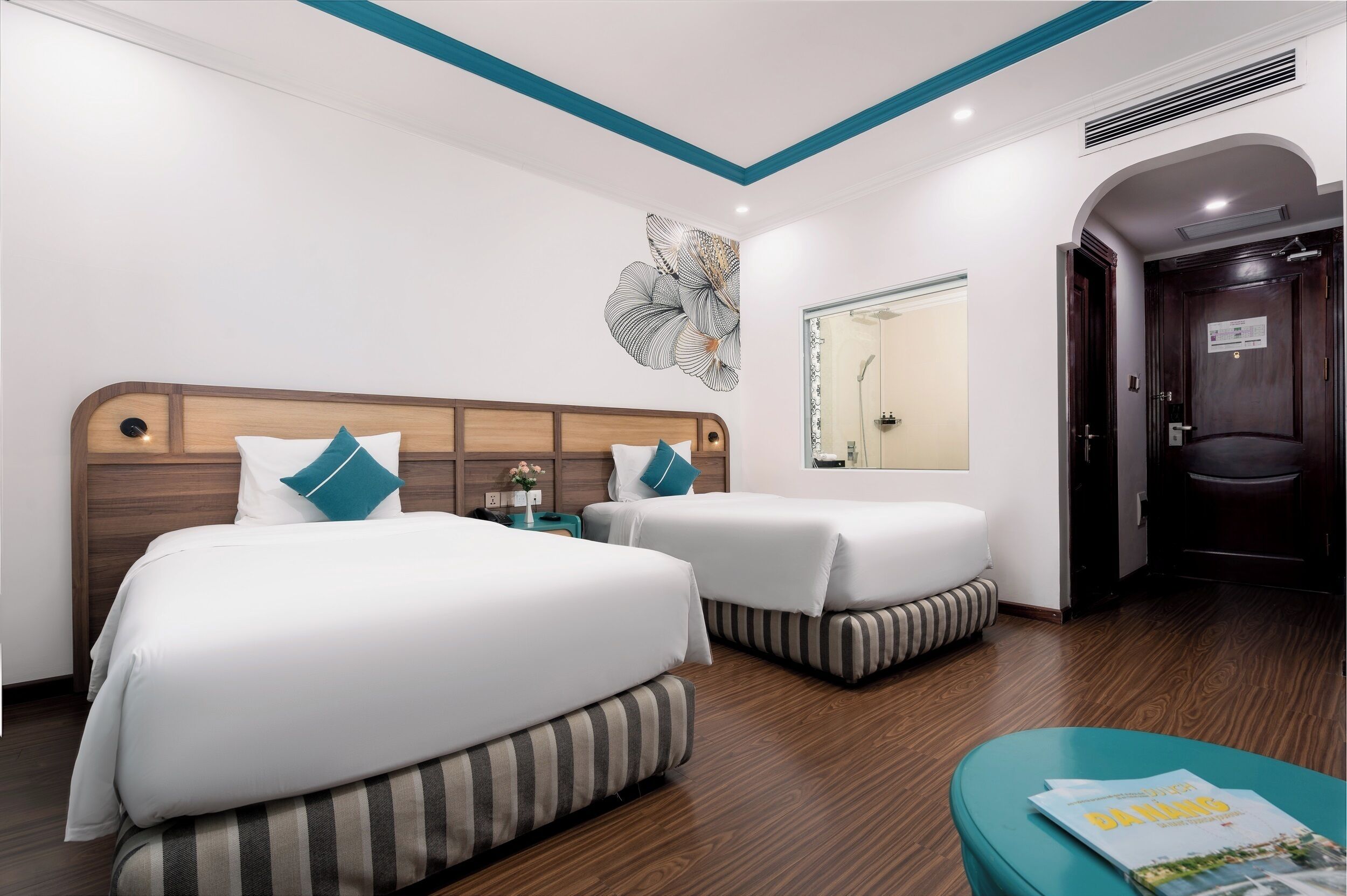 Habitación de hotel con dos camas, cabecero de madera, un espejo y una puerta.