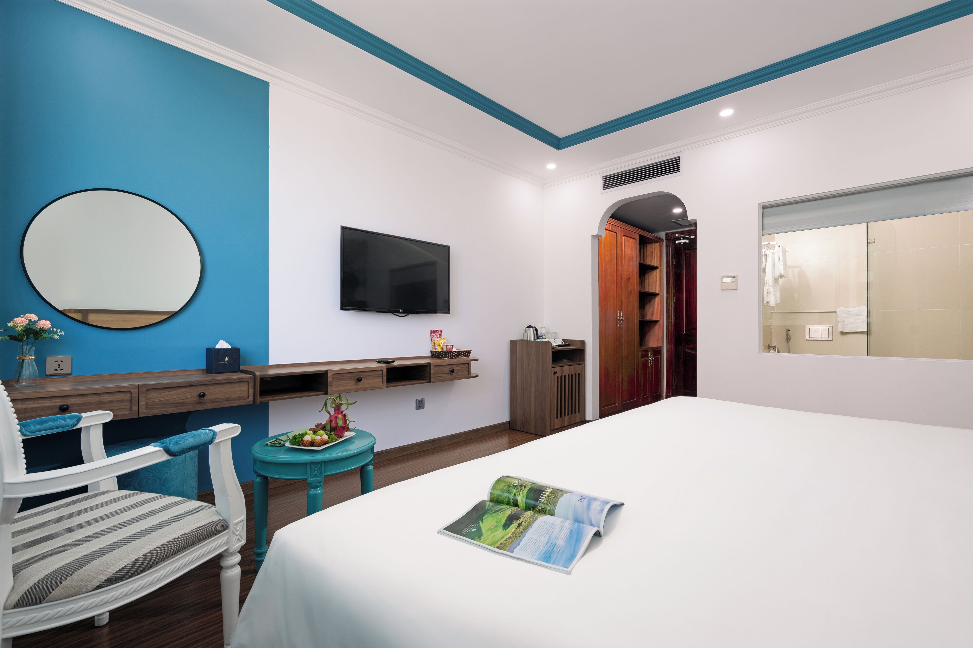 Ein Hotelzimmer mit einem Bett, einem Fernseher, einem Schreibtisch mit Stuhl, einem kleinen Tisch mit einer Vase und einem Spiegel an der Wand.