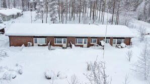 Une cabane dont le toit est recouvert de neige, entourée d’une forêt.