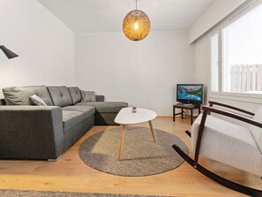 Una sala moderna con un sofá modular, una mesita redonda, un televisor y un ventanal con persianas.