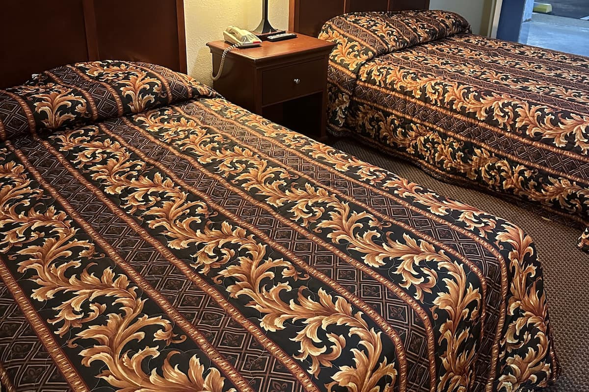 A hotel room with two beds, a nightstand with a lamp, and a door leading to the outside.