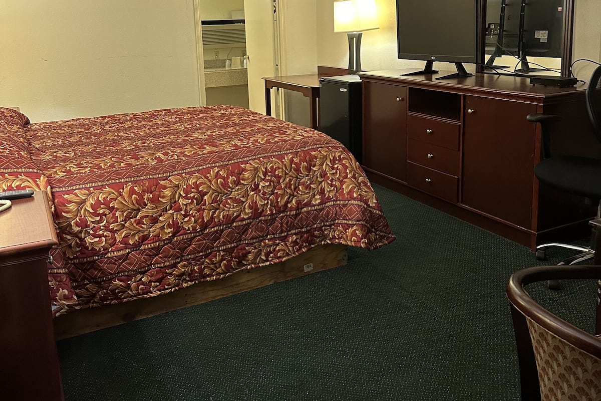 A hotel room with a large bed, a desk with a computer, a chair, a dresser, and a mirror.