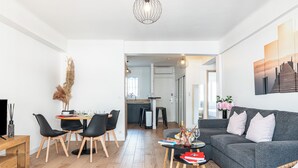 Ein modernes Wohnzimmer mit grauem Sofa, schwarzen Sesseln, einem Esstisch und einer Küche im Hintergrund.